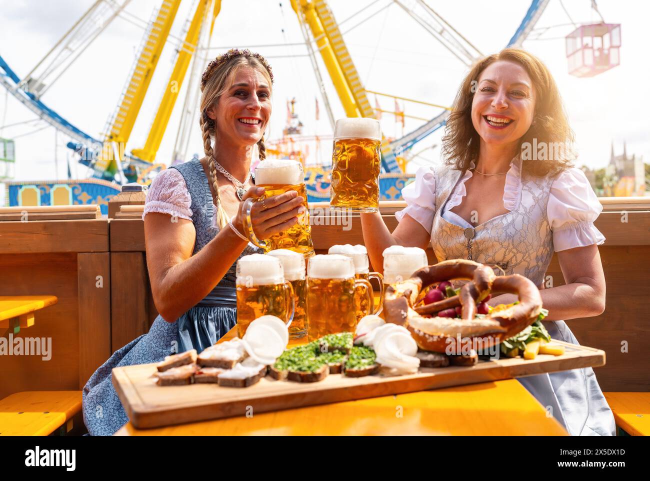 Zwei Frauen in traditionellen bayerischen Kleidern oder tracht, die mit Bierbecher und Bier und Snacks auf dem Tisch auf einem Festplatz in Bayern Oktob toben Stockfoto