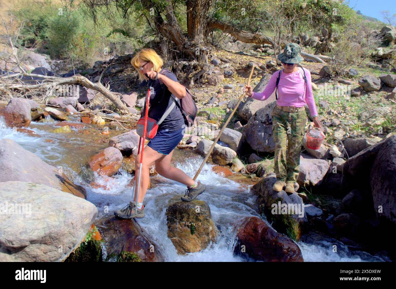 Usbekistans Ausläufer der Pamirs. Zwei weibliche Touristen überqueren einen Bergfluss. Klarer, sonniger Tag. Selektives Schärfen Stockfoto