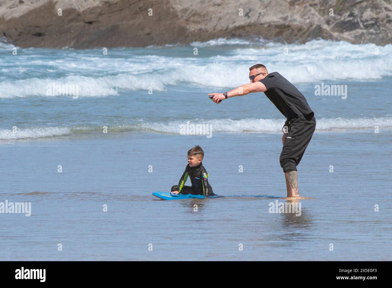 Ein Vater, der seinem Sohn hilft, ein Body Boogie Board am Fistral Beach in Newquay in Cornwall zu benutzen. Stockfoto