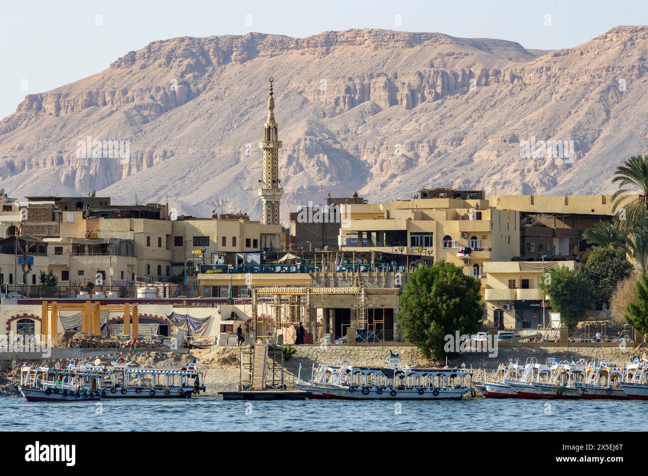 Die Stadt Luxor am Ufer des Nils in Ägypten, Afrika. Kleine Flusstaxis stehen neben dem Dock. Wüstenberg in der Ferne. Stockfoto