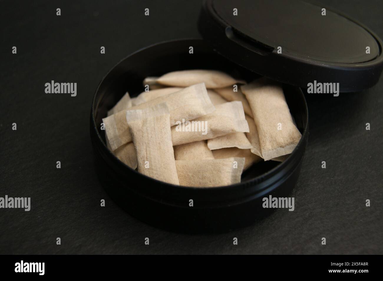 Eine offene Kiste mit Nikotinbeuteln. Nikotinpads in schwarzer Verpackung auf dunkler Oberfläche. Stockfoto