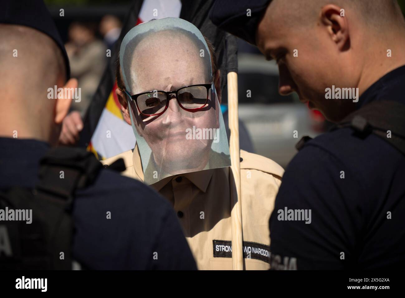 Warschau, Polen. Mai 2024. Ein Mann, der eine Maske trägt und ein Porträt des ehemaligen polnischen Staatschefs Wojciech Jaruzelski trägt, wird am 9. Mai 2024 auf dem sowjetischen Militärfriedhof in Warschau, Polen, von der Polizei festgenommen. Die Demonstranten unterbrachen den Besuch des russischen Botschafters Sergej Andrejew mit lauten Schreien, während sie Kleider trugen, die die Namen bombardierter ukrainischer Städte trugen und mit Bühnenblut bedeckt waren. (Foto: Jaap Arriens/SIPA USA) (Foto: Jaap Arriens/SIPA USA) Credit: SIPA USA/Alamy Live News Stockfoto