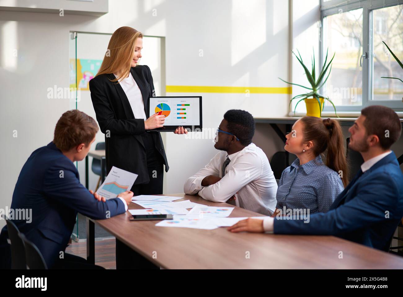 Die weibliche Führungskraft präsentiert ihren Kollegen während der Besprechung im Büro farbenfrohe Tortendiagramme auf einem Tablet. Aufmerksames Team engagiert sich in der strategischen Planung und Analyse Stockfoto