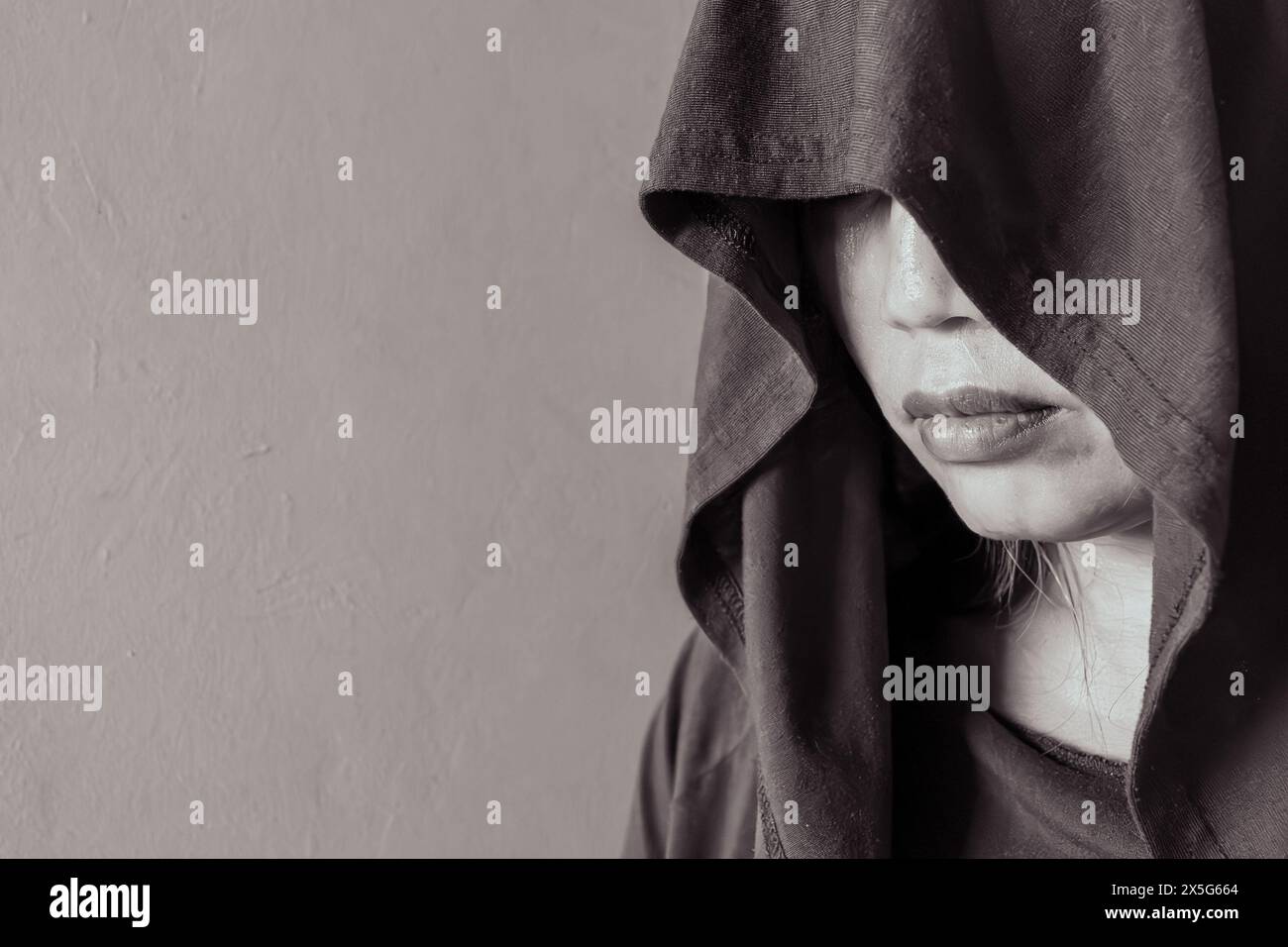 Eine Profilansicht einer Frau, die in eine Kapuze gehüllt ist. Ihr Blick ist verborgen, in krassem Schwarz-weiß Stockfoto