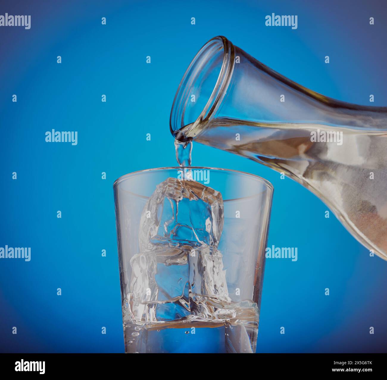 Glas mit Eisfelsen und frischem Wasser, das in das Glas gegossen wird. Stockfoto