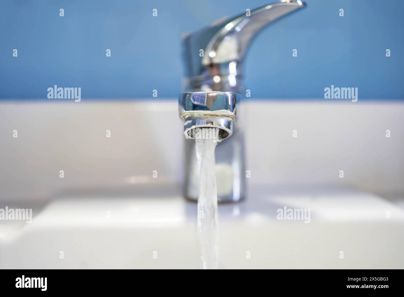 Vorderansicht des Wasserflusses aus dem Waschbecken. Altes Waschbecken mit sauberem Wasser auf blauem Hintergrund. Stockfoto