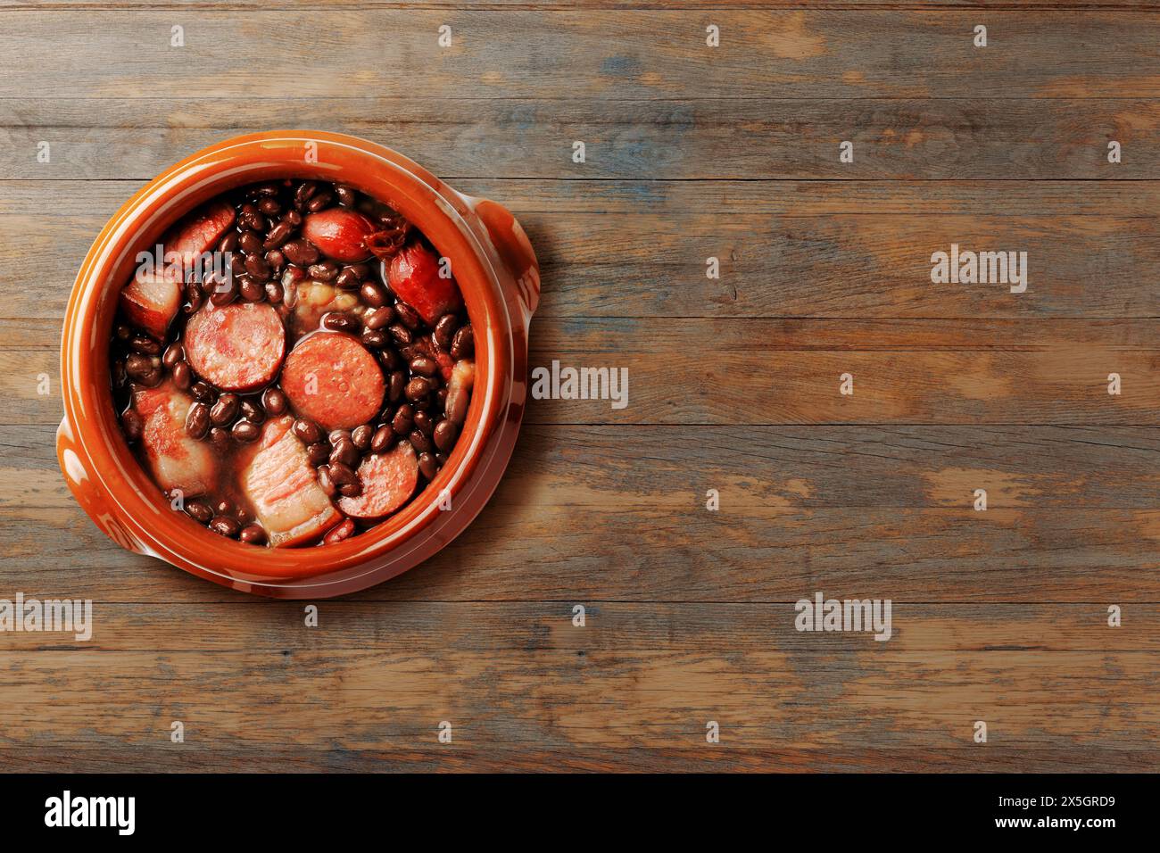 Brasilianische Feijoada, traditionelle Gerichte der brasilianischen Küche, auf Keramikauflauf, über rustikalem Holztisch. Kopierbereich. Draufsicht Stockfoto