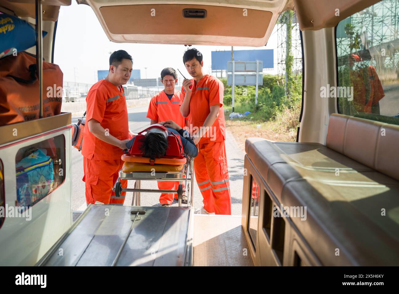 Gruppe von Sanitätern oder Notfallmedizinern (EMT) in einer orangen Uniform platziert ein Nacken-Kopf-Unfallopfer in einem Krankenwagen auf ein Bett. Dringend Stockfoto