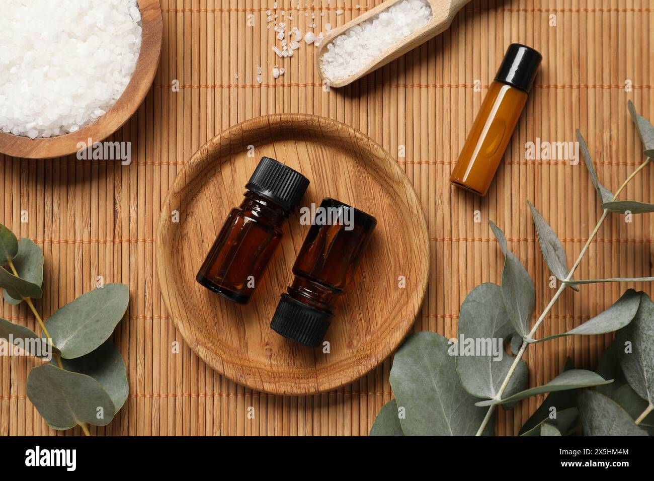 Aromatherapieprodukte. Flaschen mit ätherischem Öl, Meersalz und Eukalyptuszweigen auf Bambusmatte, flach liegend Stockfoto
