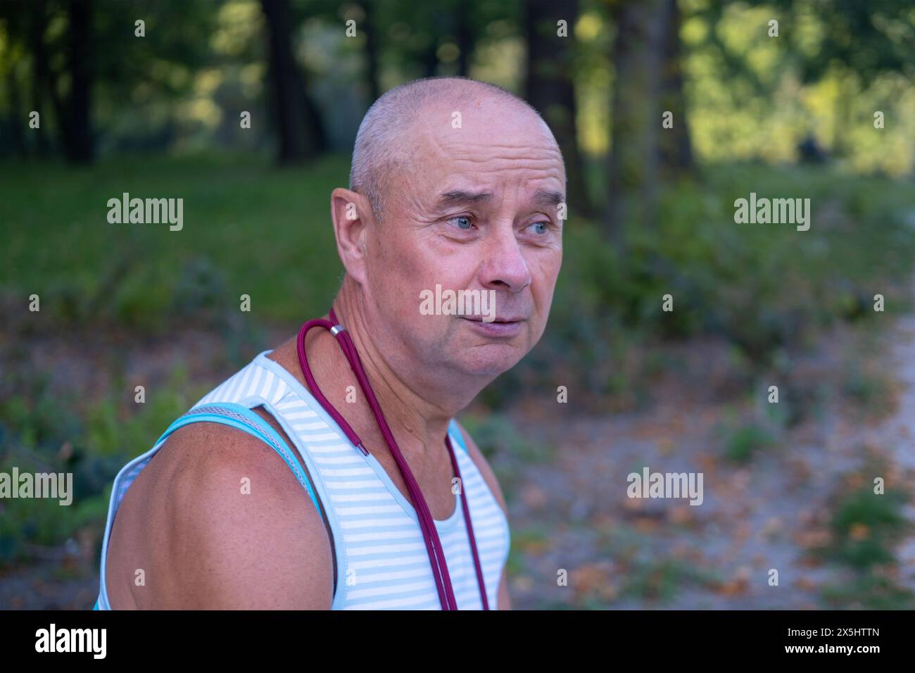 Nahaufnahme männliches Gesicht, hübscher kaukasischer reifer Mann 60-65 Jahre alt, lächelnd auf grünem natürlichem Hintergrund, gute Stimmung, altersbedingte Veränderungen, Konzept mentale hu Stockfoto