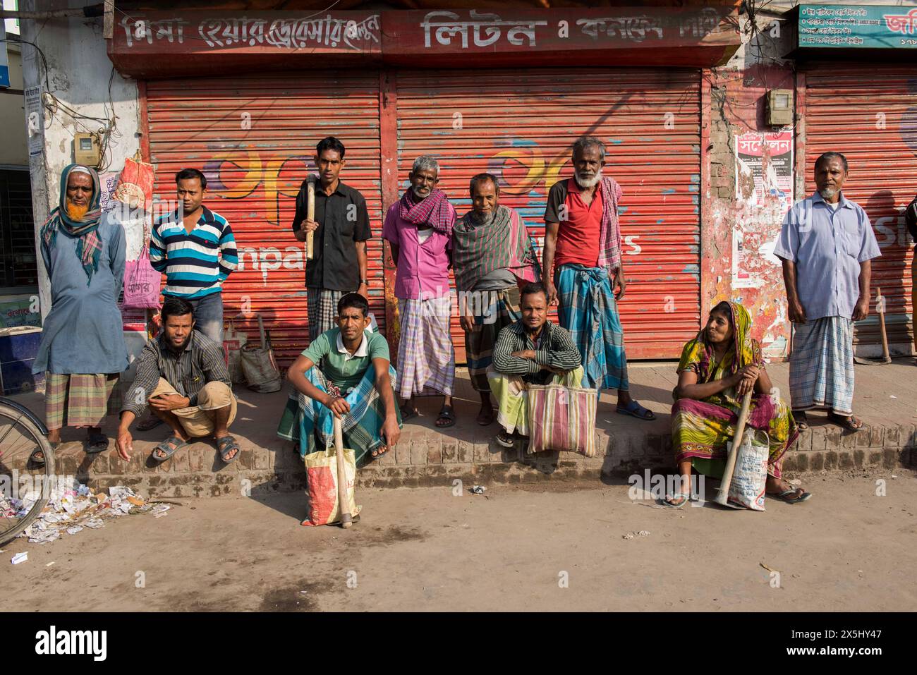 Bangladesch, Jhenaidah. Tagelöhner mit ihren Werkzeugen, Männer und Frauen, stehen am Straßenrand und suchen Arbeit. (Nur für redaktionelle Zwecke) Stockfoto