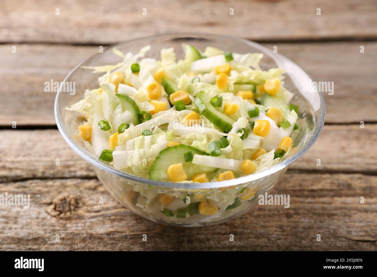 Leckerer Salat mit Chinakohl, Mais und Gurke in Schüssel auf Holztisch, Nahaufnahme Stockfoto