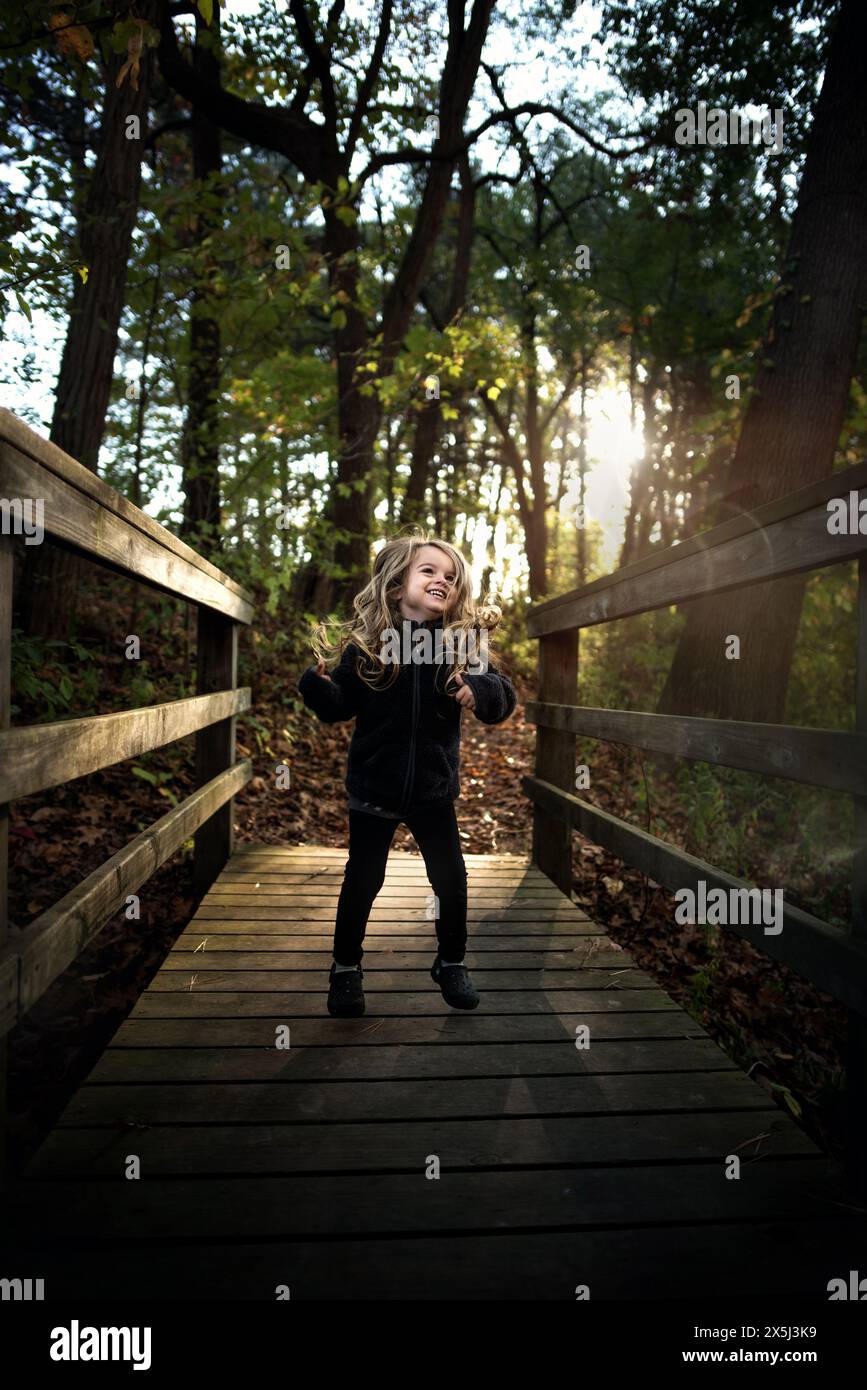 Kleines Mädchen, das auf einer Holzbrücke im Wald läuft und lächelt Stockfoto