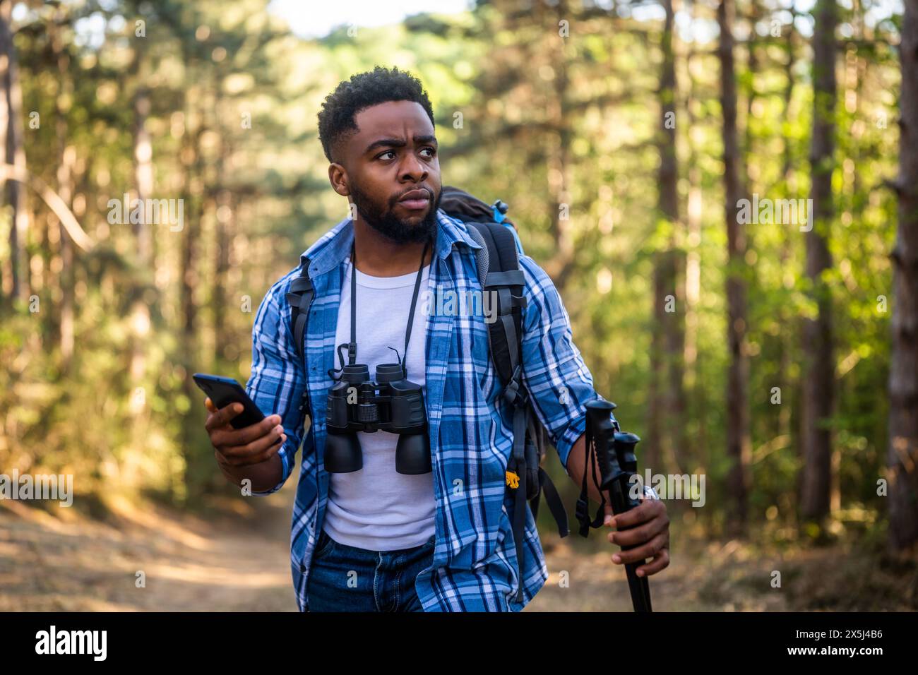 Ein besorgter Wanderer hat sich verirrt und er benutzt ein Telefon, um die richtige Richtung zu finden, während er in der Natur wandert. Stockfoto