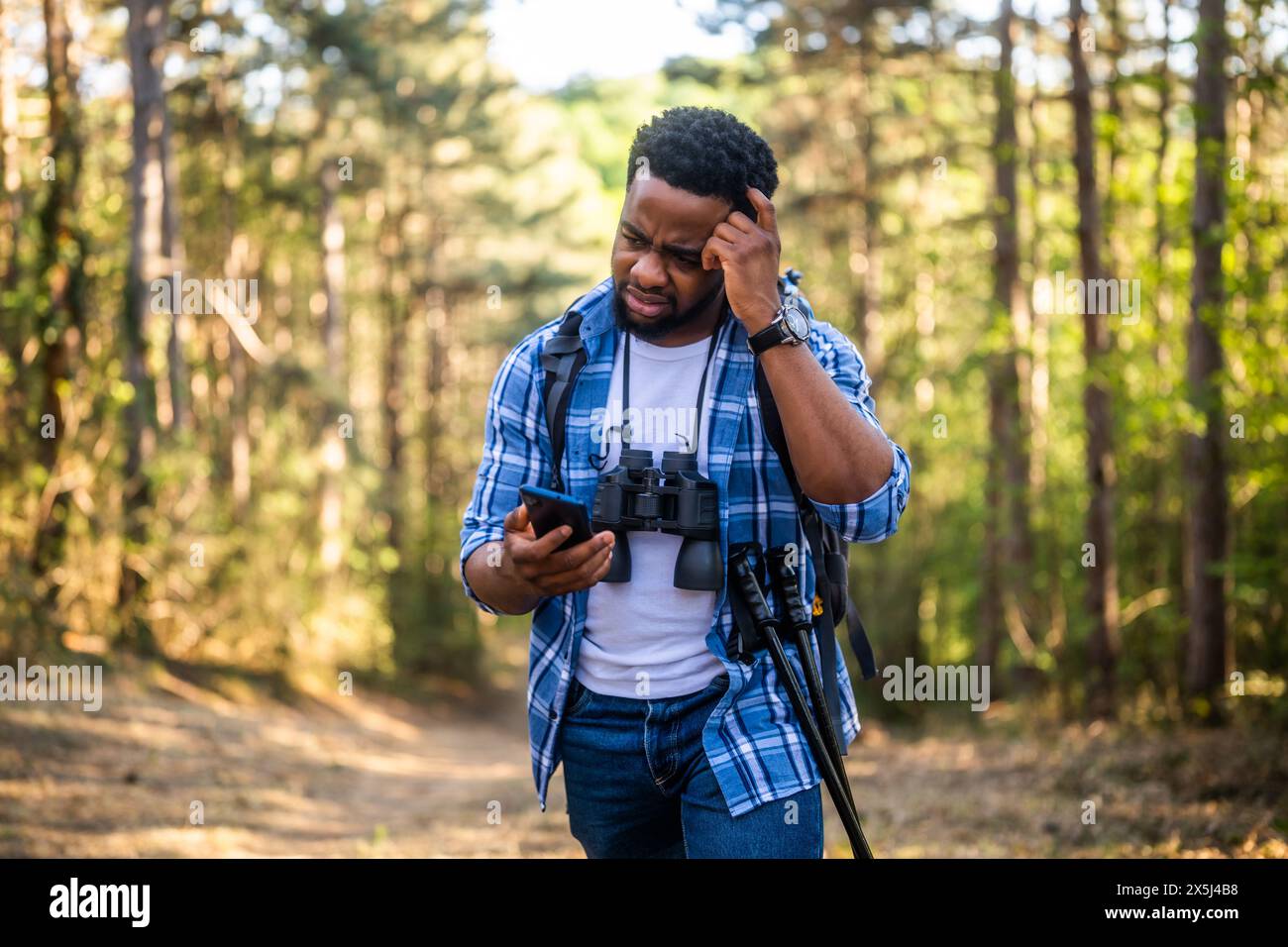 Ein besorgter Wanderer hat sich verirrt und er benutzt ein Telefon, um die richtige Richtung zu finden, während er in der Natur wandert. Stockfoto