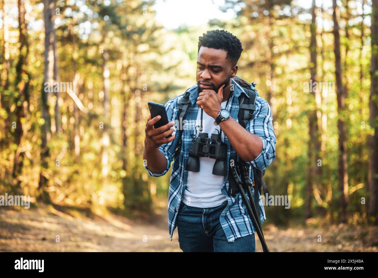 Ein besorgter Wanderer hat sich verirrt und er benutzt ein Telefon, um die richtige Richtung zu finden, während er in der Natur wandert. Stockfoto