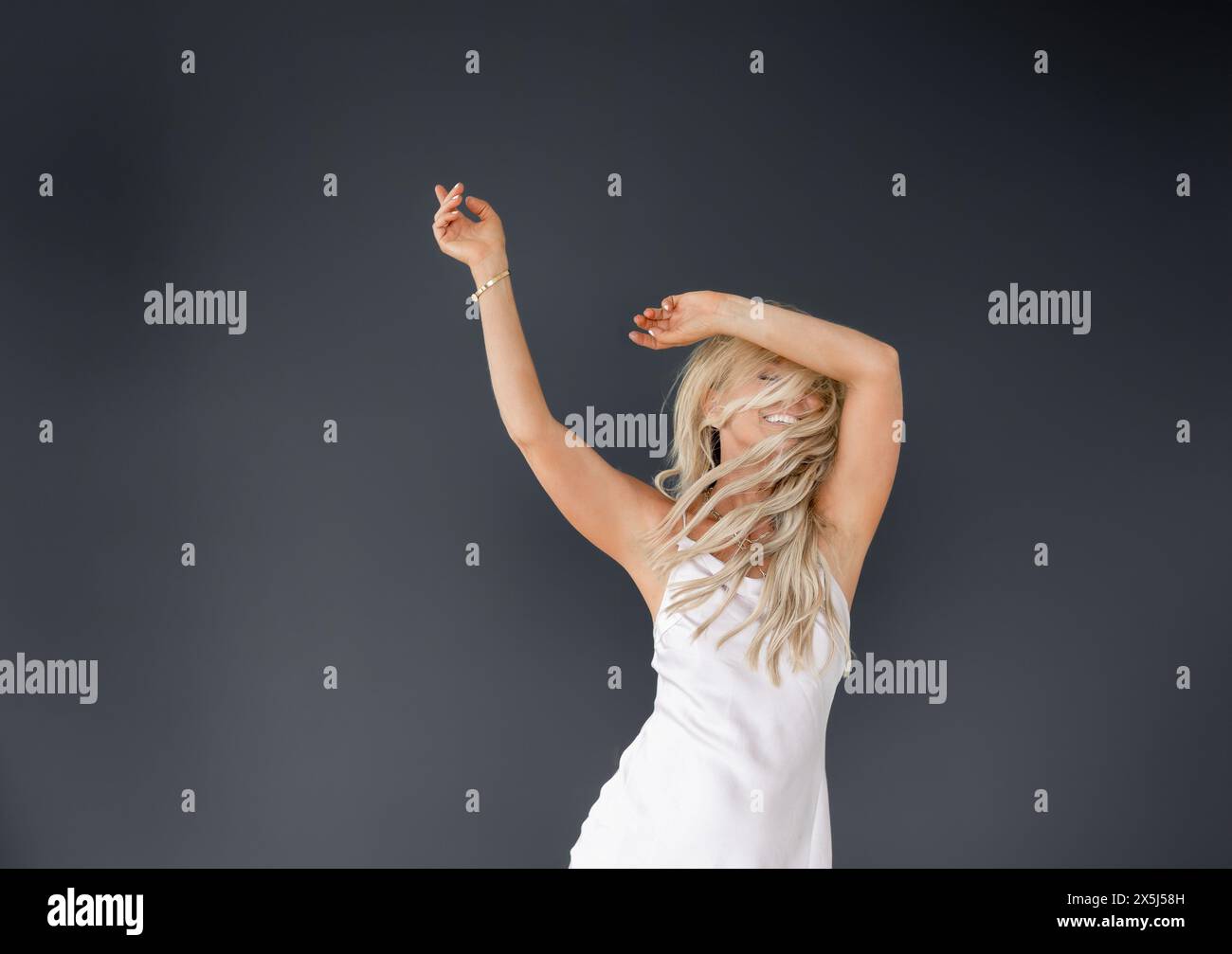 Fröhliche Frau in weißem Kleid, die auf dunklem Hintergrund tanzt Stockfoto