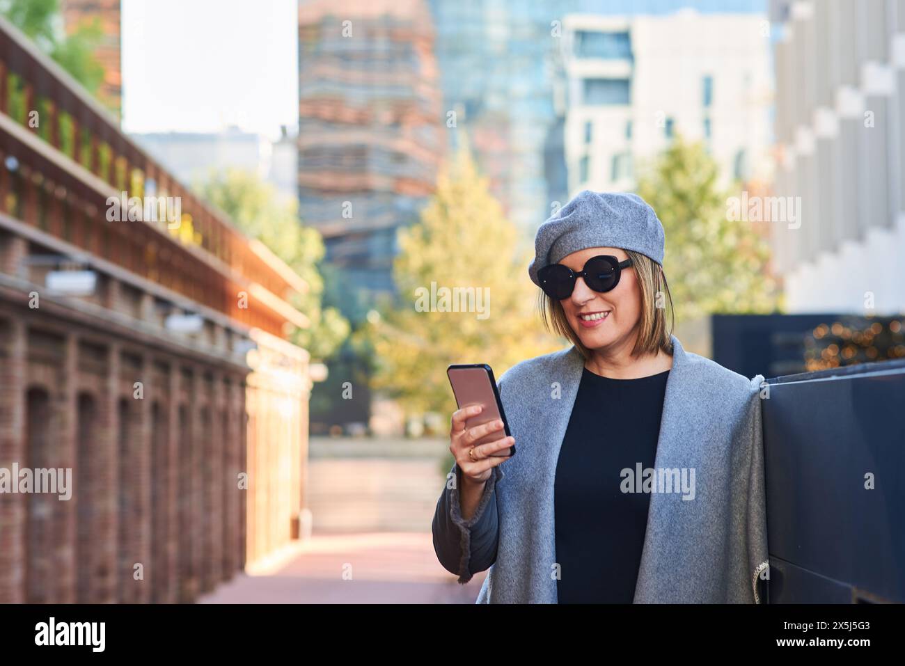 Fröhliche Frau mit Smartphone in urbaner Herbstkulisse Stockfoto