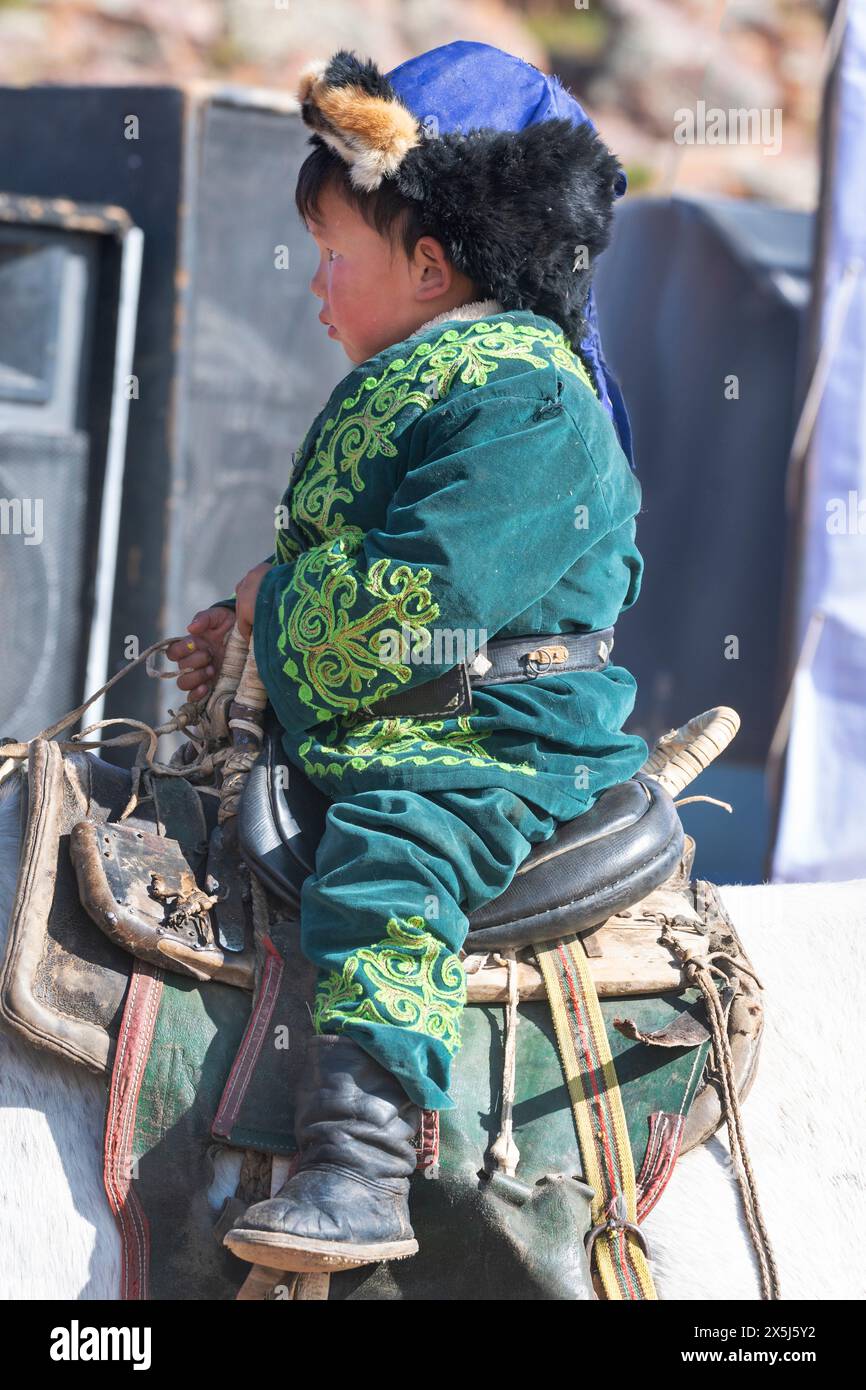 Asien, Mongolei, Provinz Bayan-Oglii. Altai Eagle Festival, kasachisches Kleinkind in traditioneller bestickter Kleidung sitzt in einem Sattel. (Nur Für Redaktionelle Zwecke) Stockfoto
