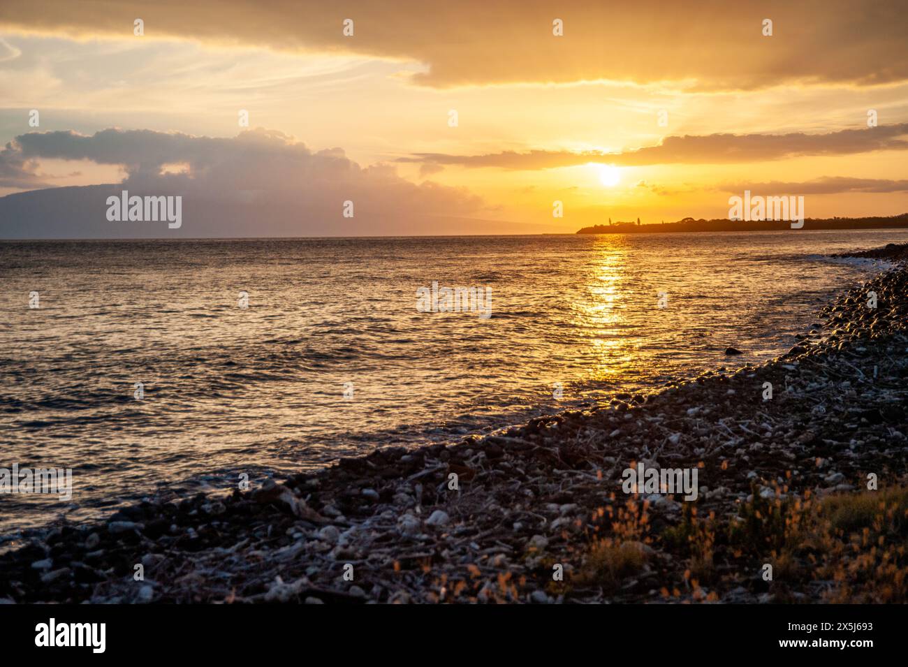 Der hawaiianische Sonnenuntergang wirft ein warmes Licht auf das Meer und die Kieselküste Stockfoto