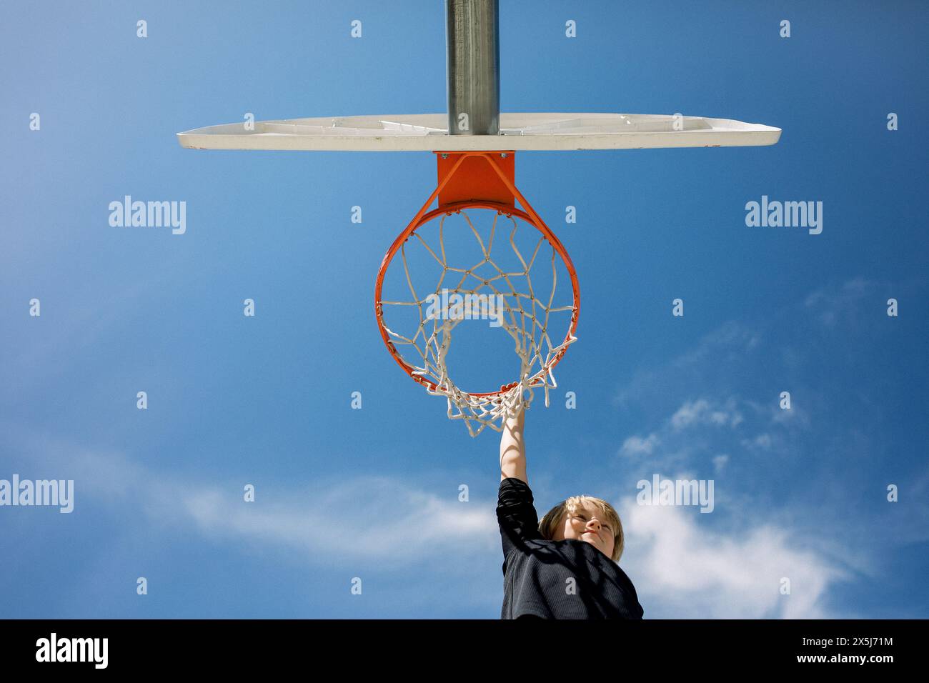 Der Junge greift nach einem Basketballkorb unter blauem Himmel Stockfoto