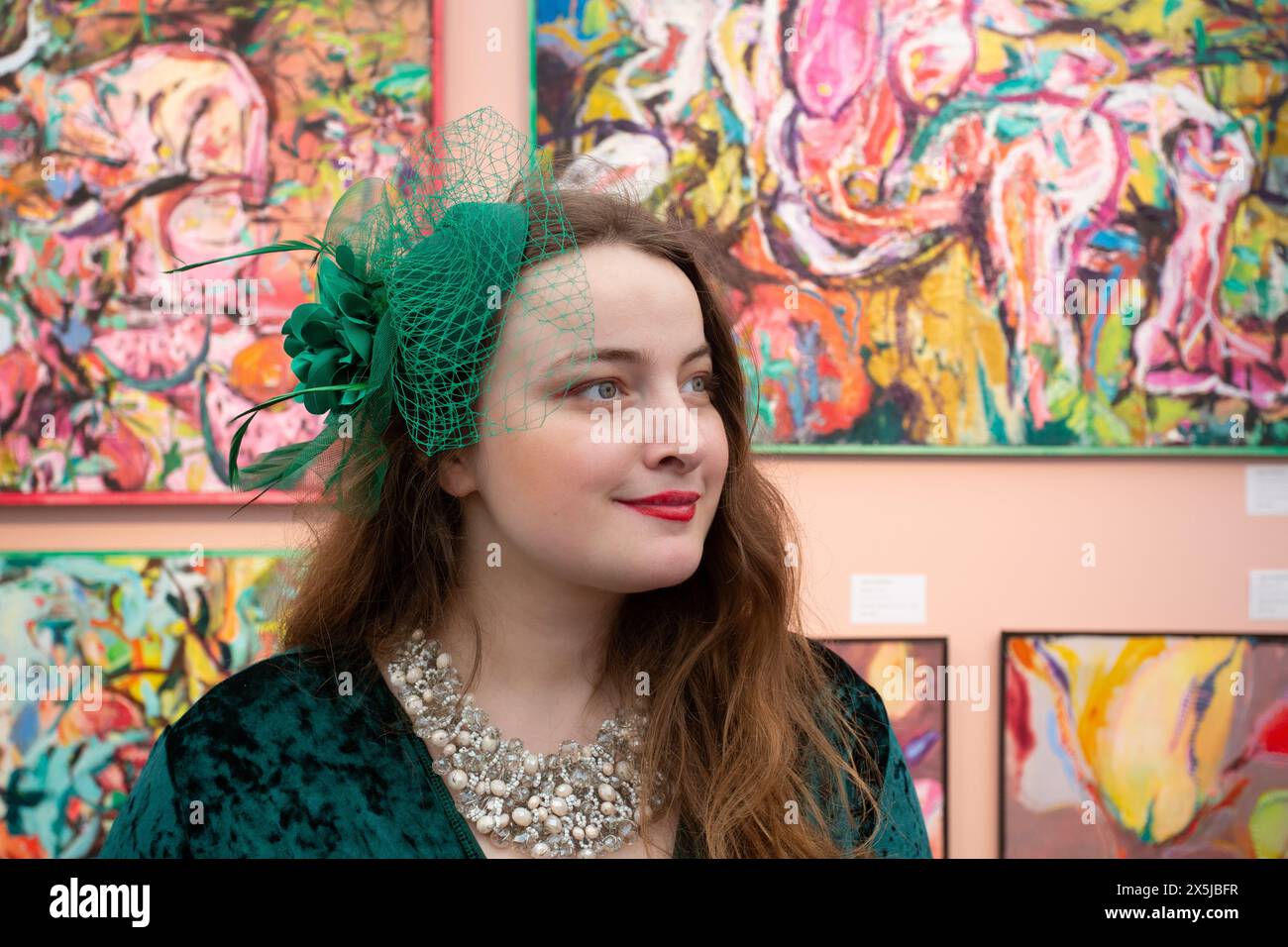 Junge Frau mit Hut, die Gemälde am Eröffnungstag der Kunstmesse beobachtet. Stockfoto