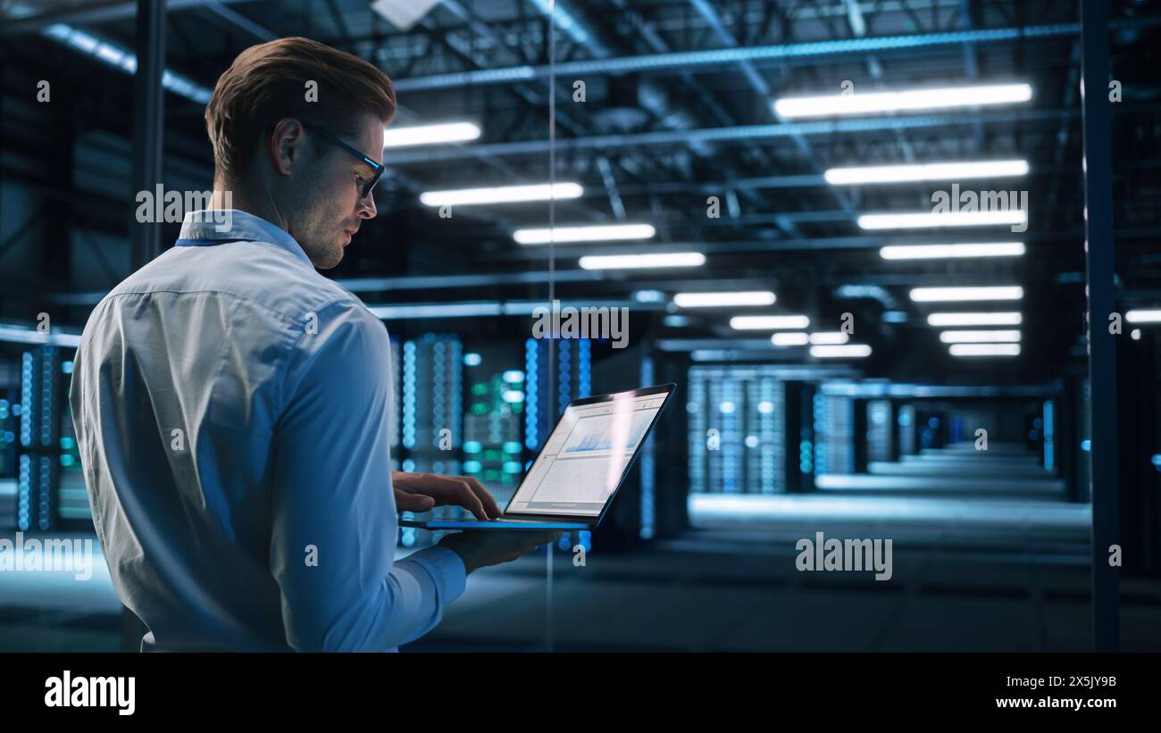 Männlicher IT-Spezialist für Rechenzentren, der ein Notebook während der Arbeit am Computer verwendet. It-Experte. Konzept für Cloud Computing und Cyber Security Maintenance Stockfoto