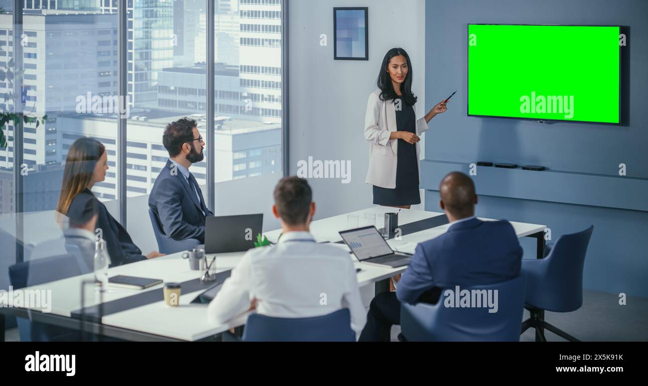 Meeting im Konferenzraum in diversen Büros: Die asiatische weibliche Projektmanagerin nutzt Green Screen Chroma Key Wall TV, um digitale Investitionsmöglichkeiten für das Happy Investment Team zu präsentieren. Stockfoto
