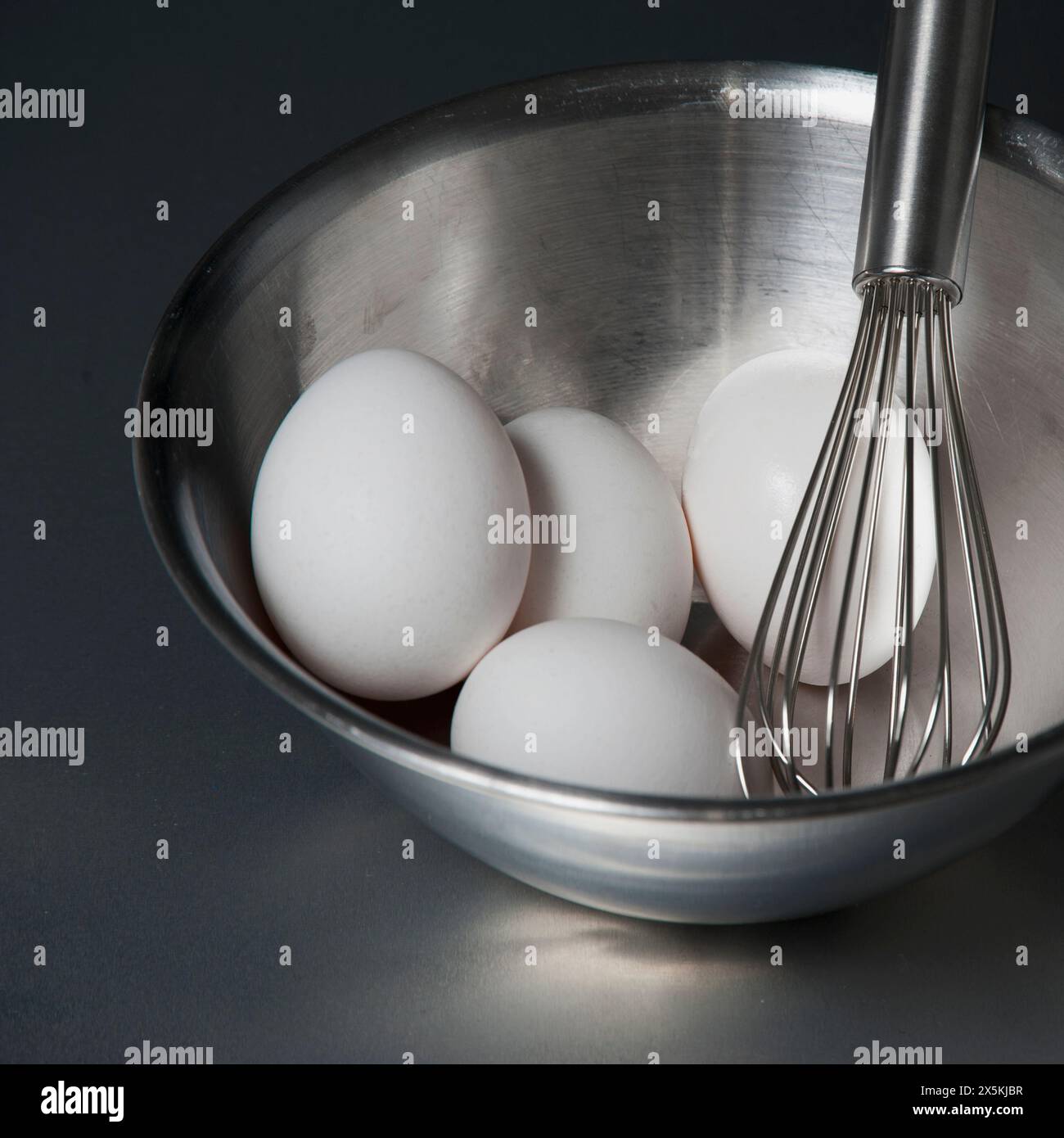 Eine Metallschale mit einem Schneebesen und weißen Eiern. Stockfoto