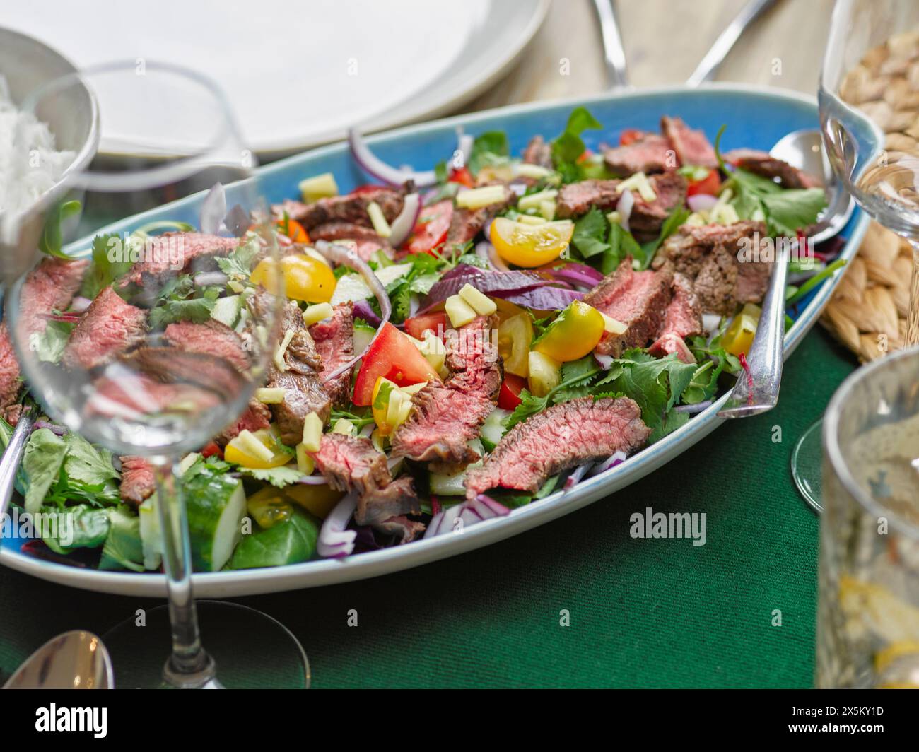 Asiatischer Salat mit thailändischen Chili-Rindfleischscheiben und Weinglas auf dem Tisch Stockfoto