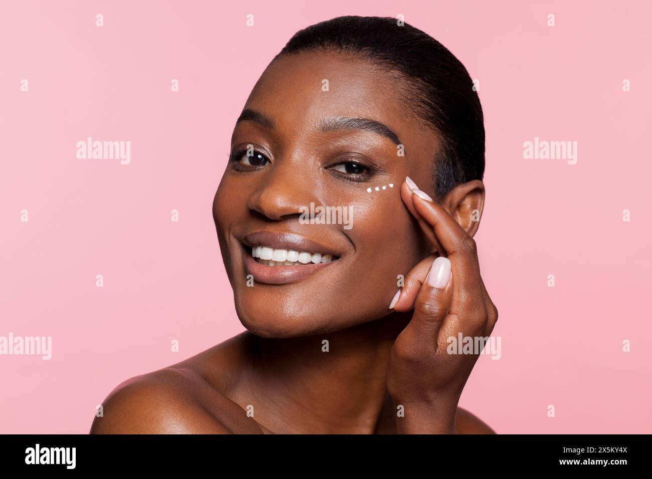 Lächelnde junge Frau, die Augencreme aufträgt Stockfoto