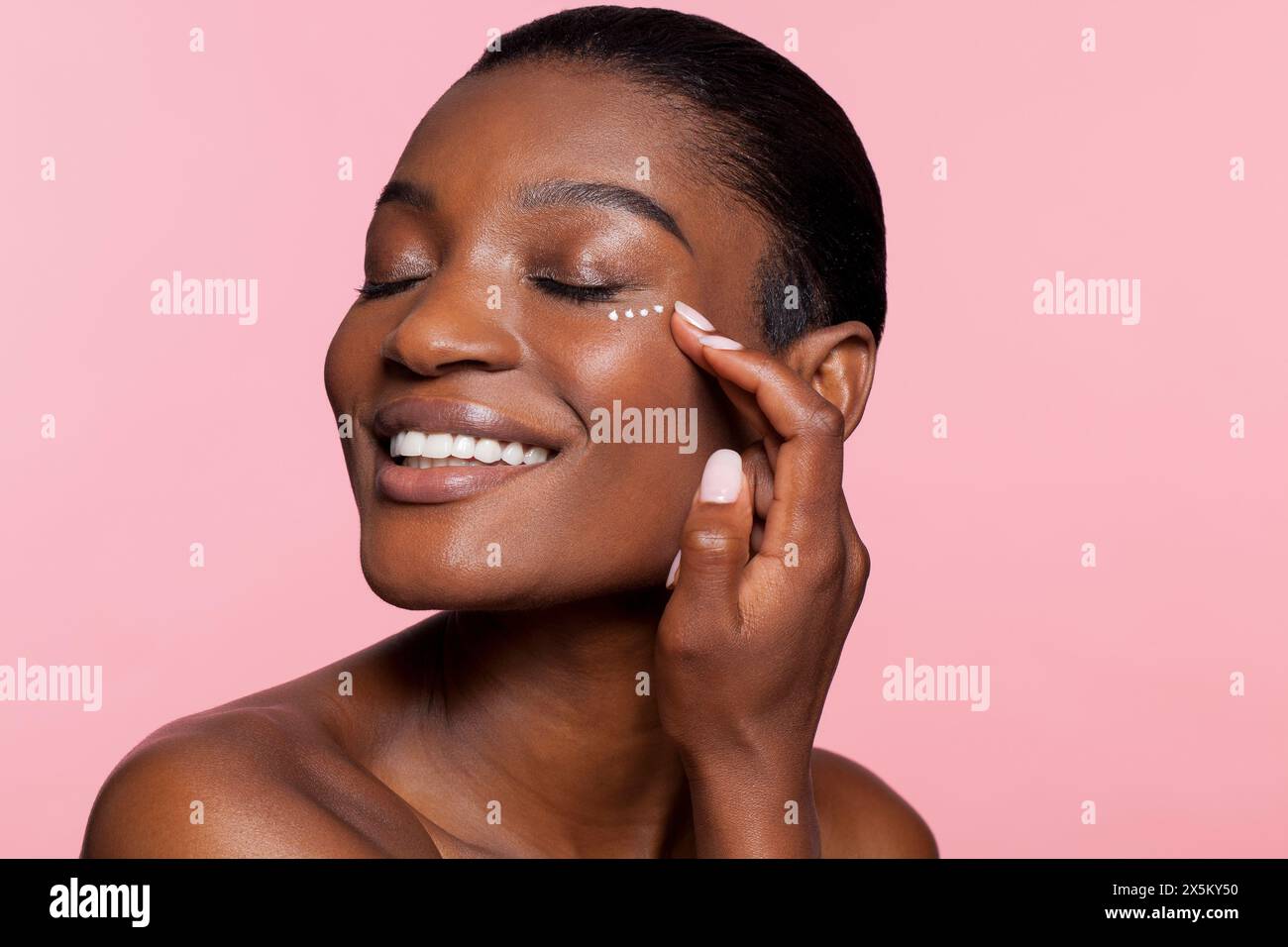 Lächelnde junge Frau, die Augencreme aufträgt Stockfoto
