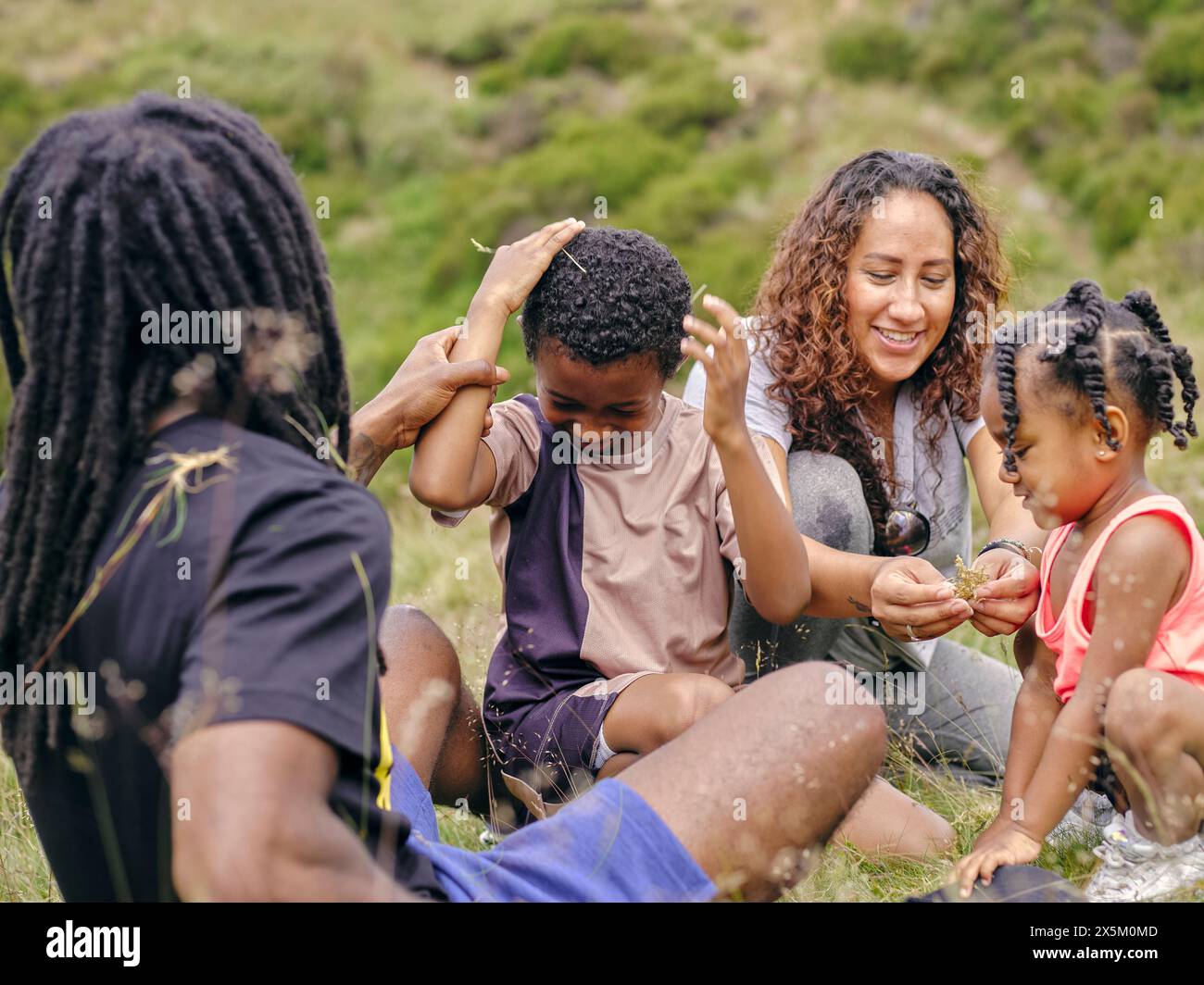Familie mit zwei Kindern, die im Gras sitzen und zusammen spielen Stockfoto