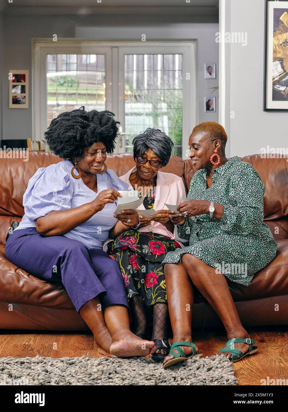 Frauen und ältere Mutter sitzen auf dem Sofa und schauen sich Fotos an Stockfoto