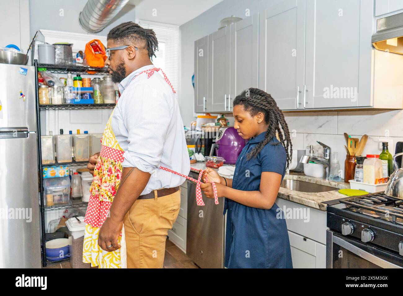 Mädchen, das Vater hilft, Schürze in der Küche zu binden Stockfoto