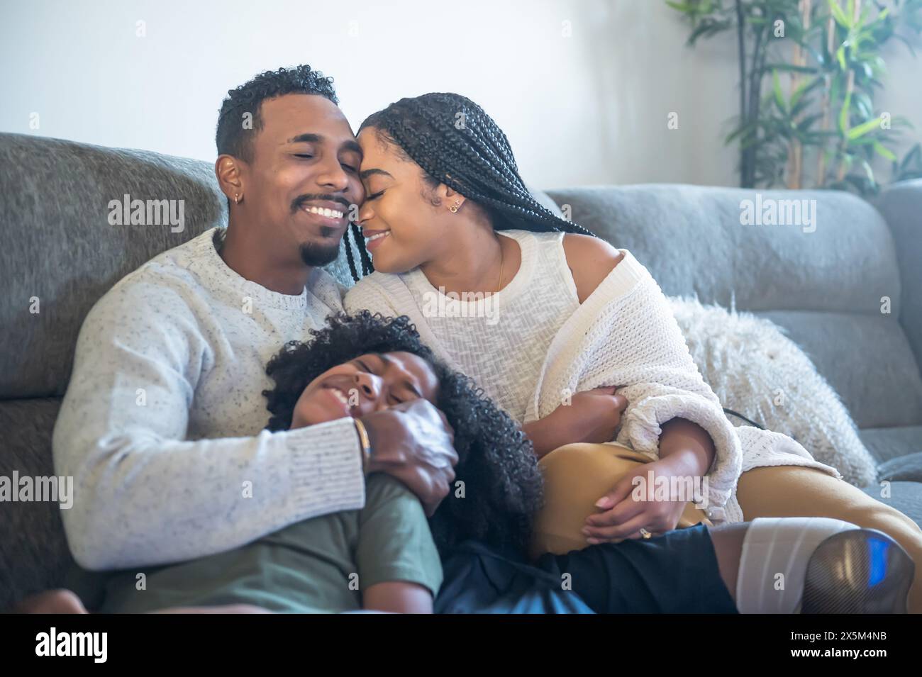 Mutter und Vater mit Prothesen, die den Sohn auf dem Sofa umarmen Stockfoto