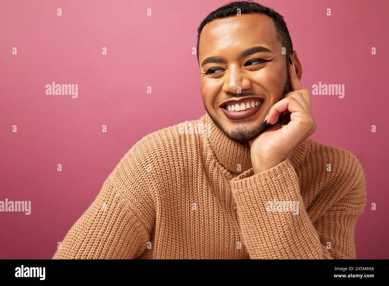 Studio-Porträt eines lächelnden queeren Mannes vor violettem Hintergrund Stockfoto