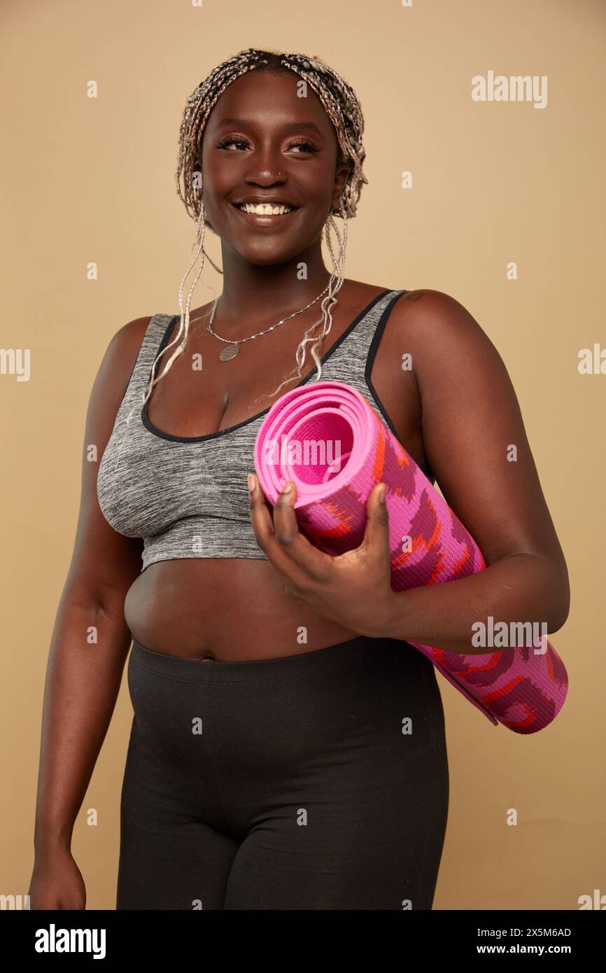 Studio-Porträt einer lächelnden und großen Frau mit Trainingsmatte Stockfoto