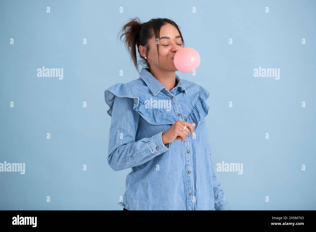 Studio-Aufnahme einer jungen Frau, die Kaugummi kaut und Blase bläst Stockfoto