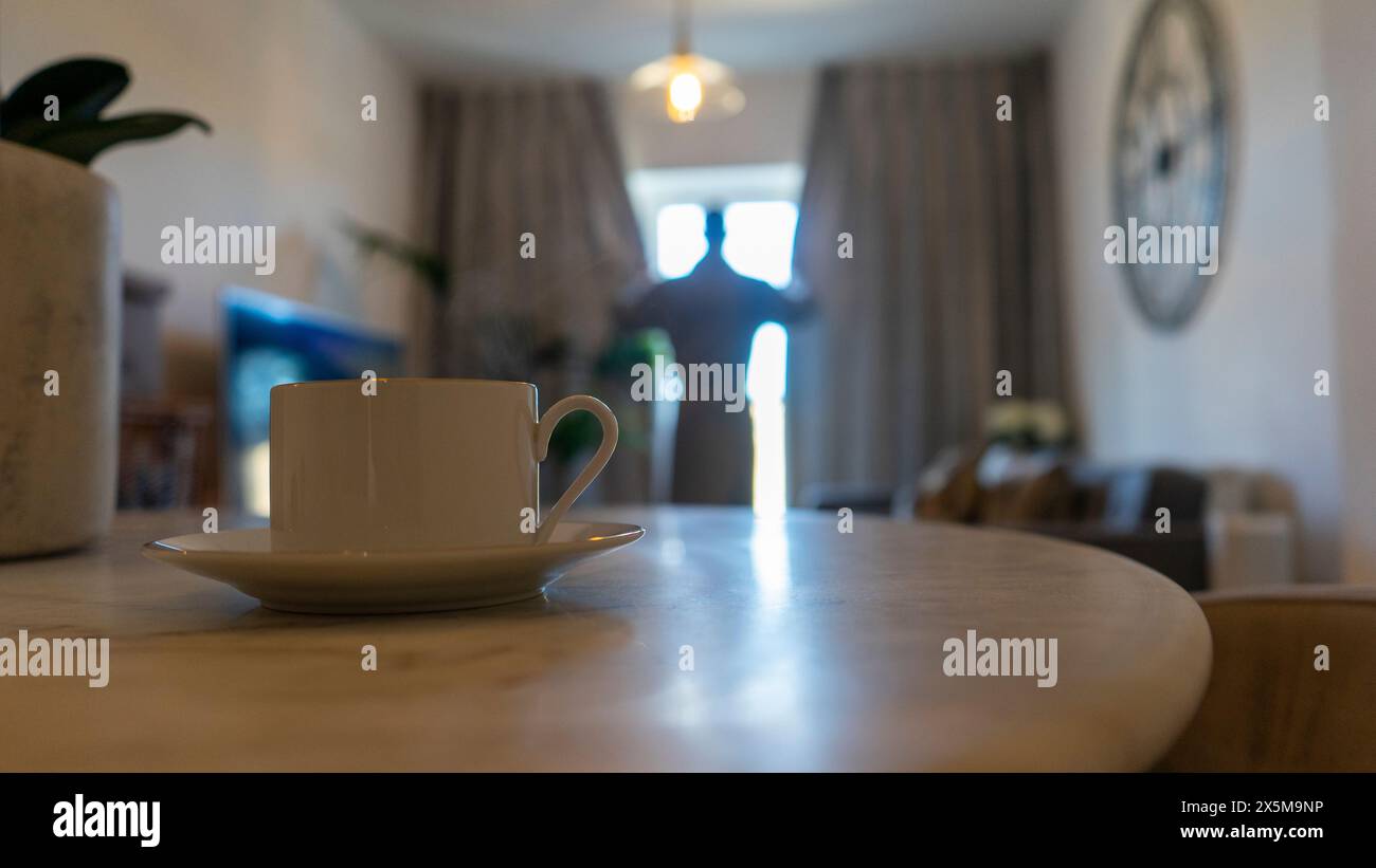 Mann im Wohnzimmer, Fokus auf Kaffeetasse im Vordergrund Stockfoto