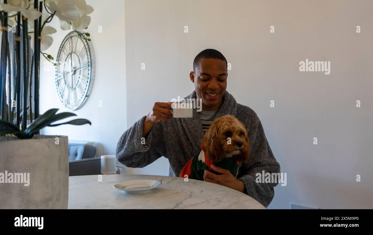 Mann sitzt am Tisch und hält Hund auf dem Schoß Stockfoto