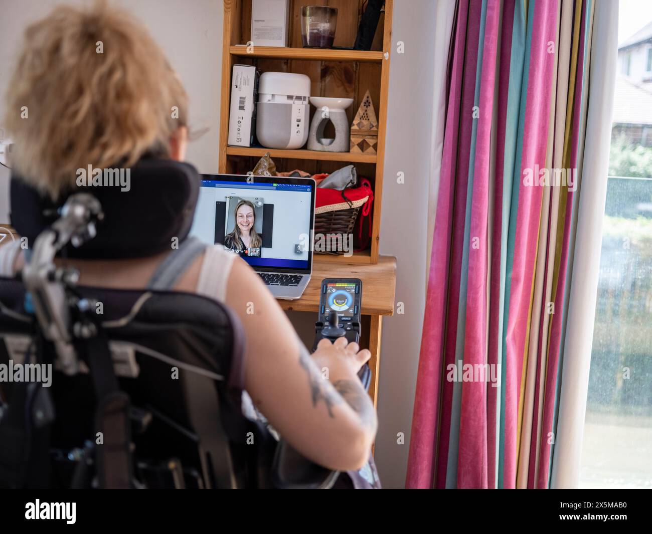 Frau im elektrischen Rollstuhl mit Videoanruf auf Laptop Stockfoto