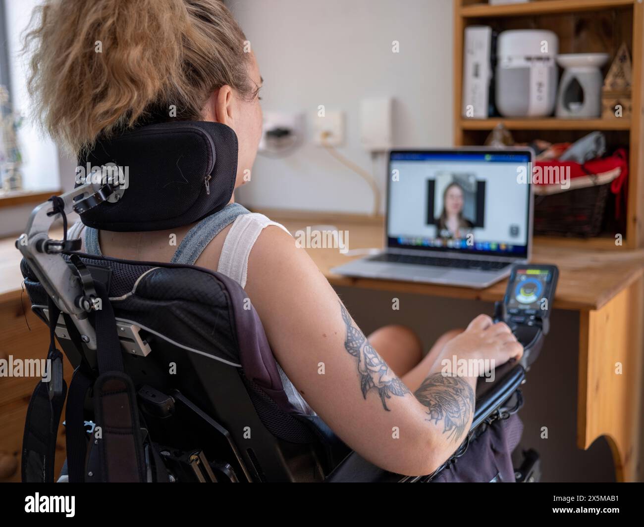 Frau im elektrischen Rollstuhl mit Videoanruf auf Laptop Stockfoto