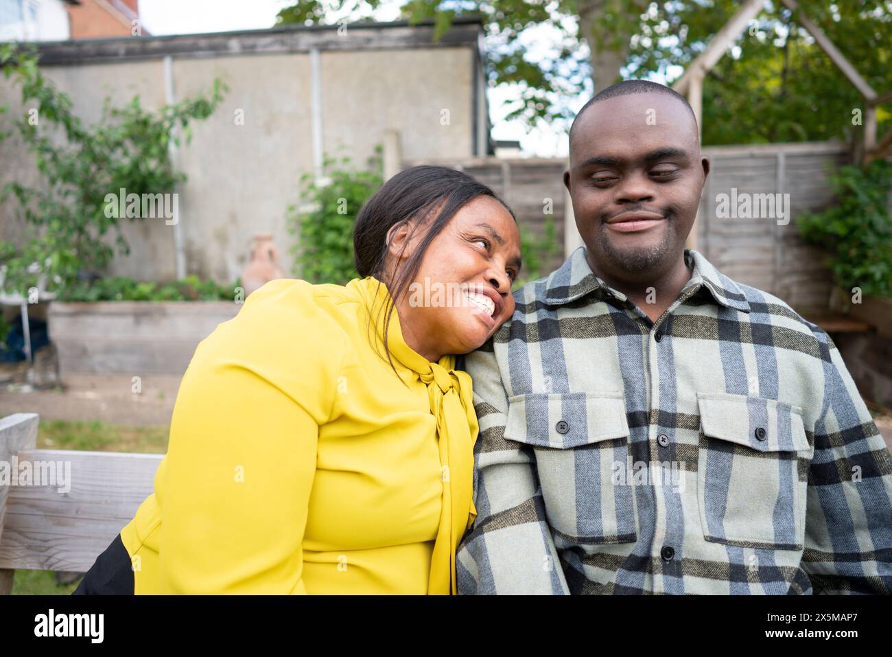Mutter und erwachsener Sohn mit Down-Syndrom, die auf einer Bank im Garten sitzen Stockfoto
