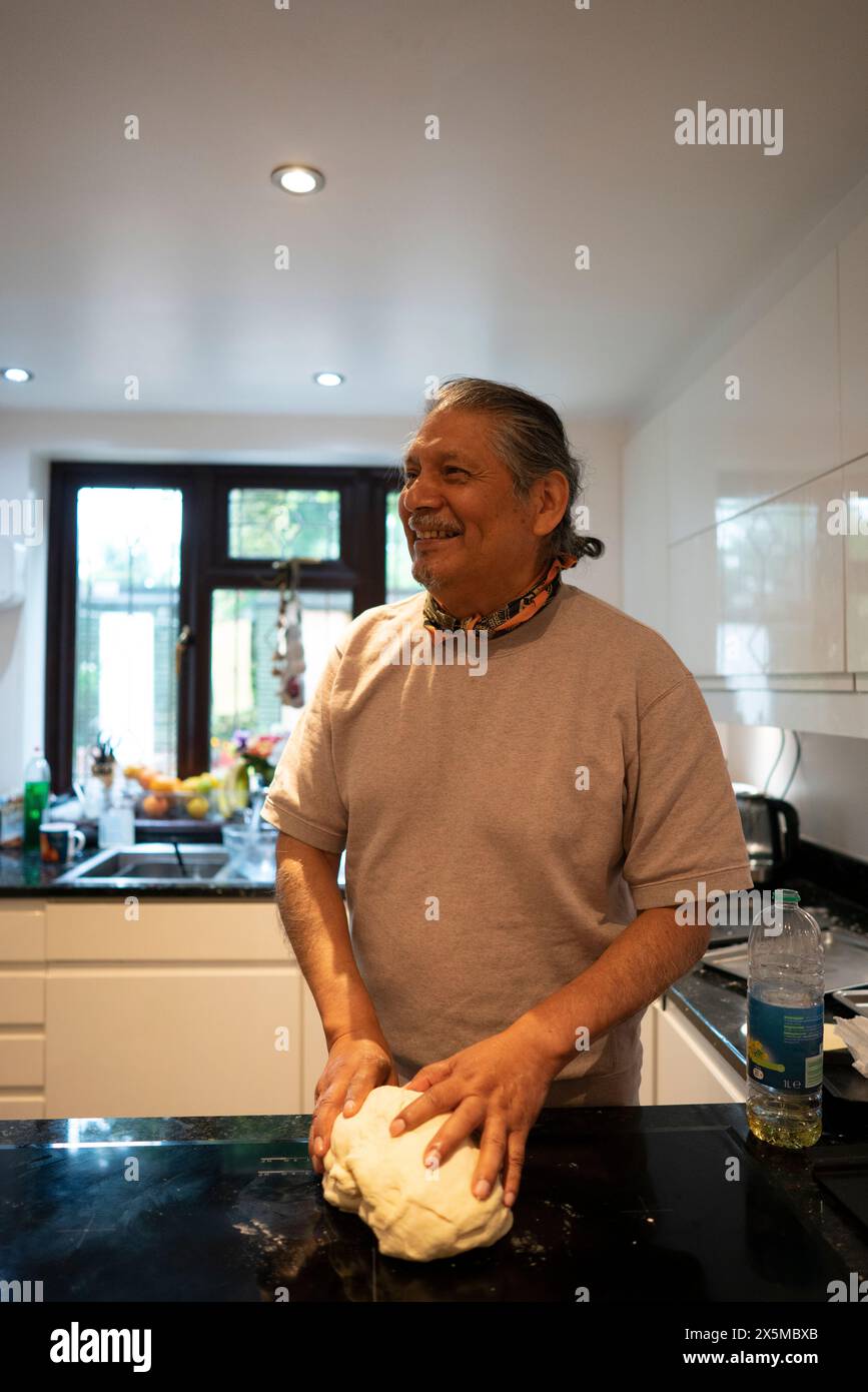 Lächelnder Senior-Mann, der Pizzateig in der Küche macht Stockfoto