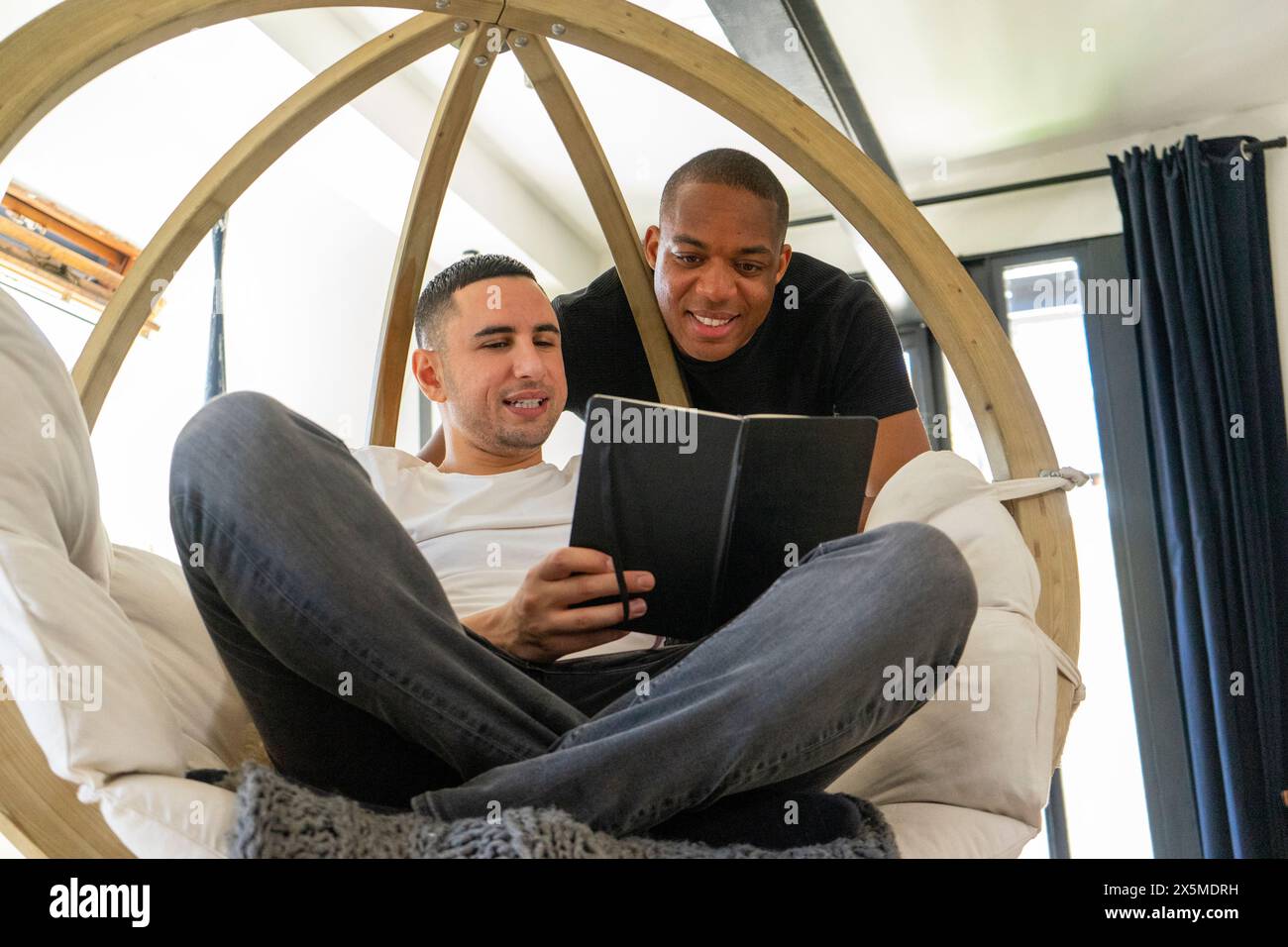 Großbritannien, London, ein lächelndes schwules Paar, das im Wohnzimmer ein Notebook ansieht Stockfoto