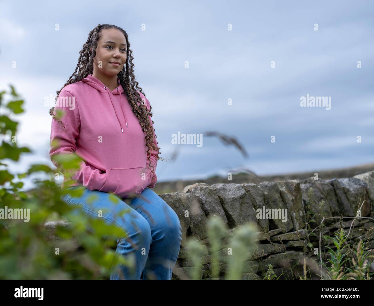 Teenager (16-17) Mädchen, das auf einer Steinmauer sitzt Stockfoto