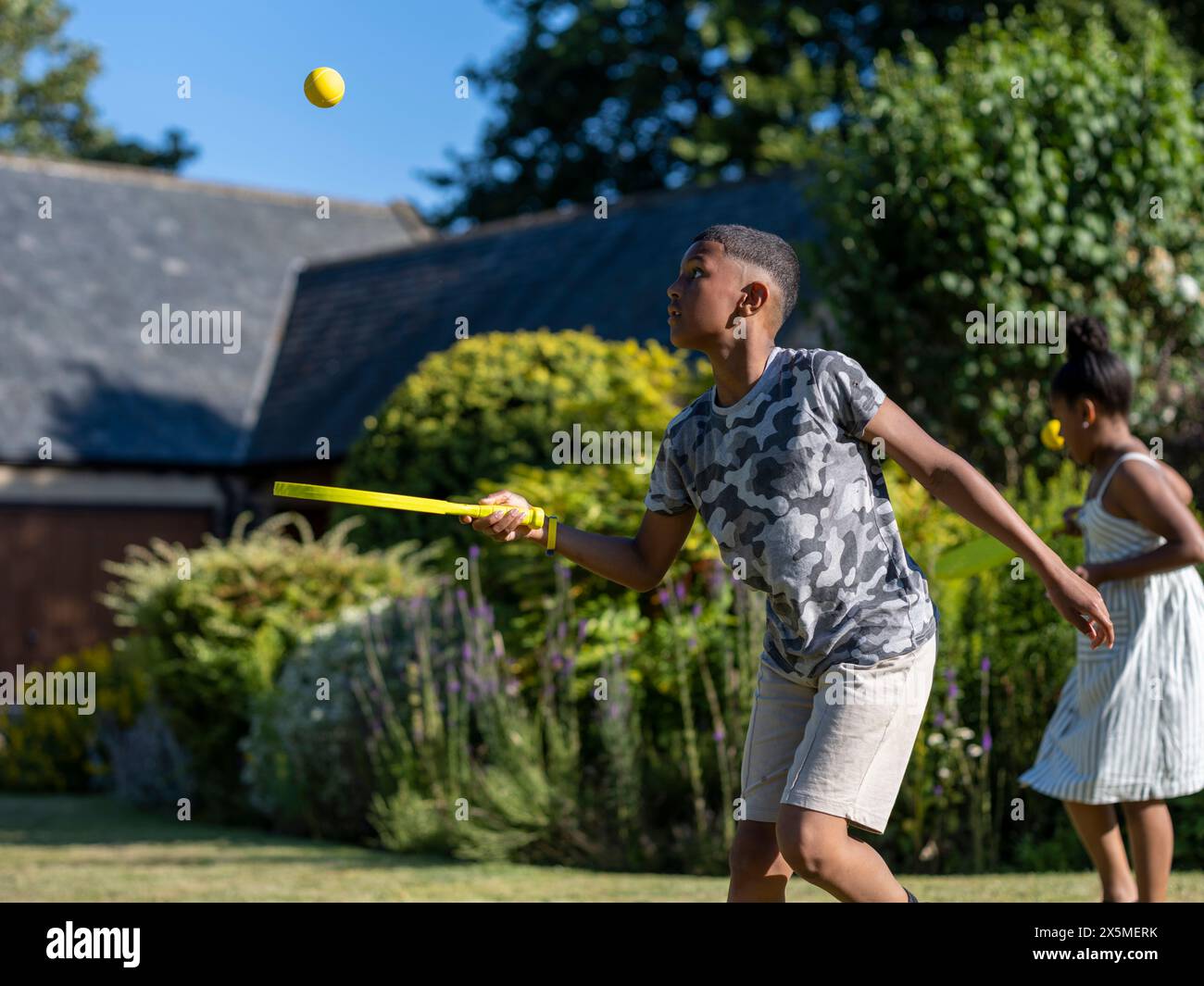 Geschwister (8-9, 10-11) spielen Paddelball im Garten Stockfoto