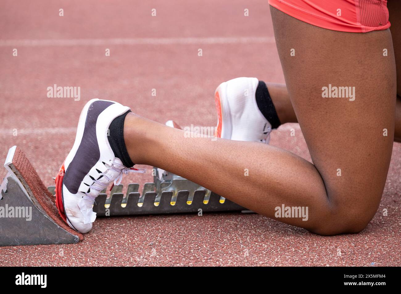 Nahaufnahme weiblicher Läuferbeine in Startposition auf Laufbahn Stockfoto