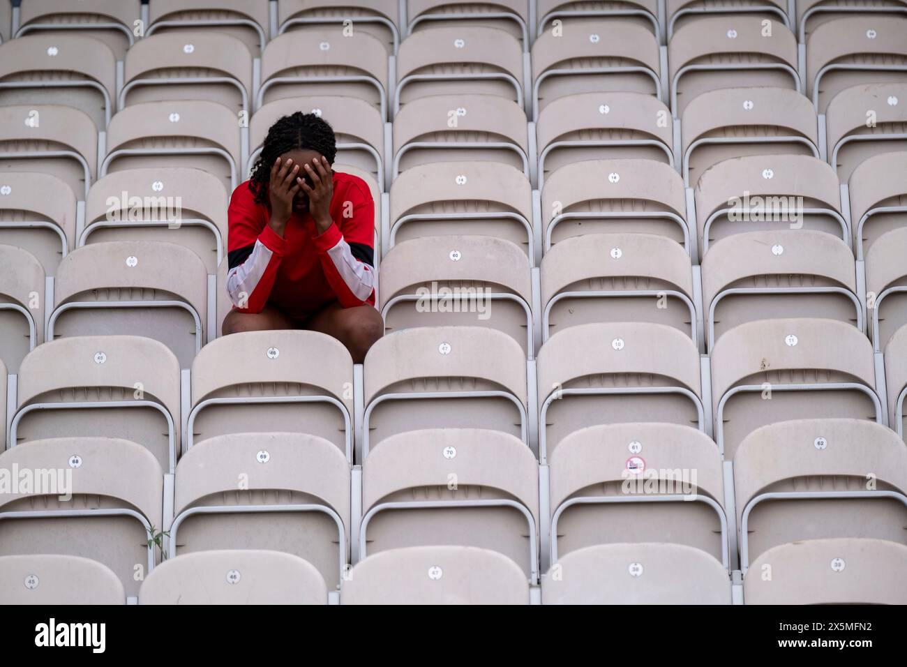 Athletische Frau mit Kopf in den Händen, die auf einem Stuhl im leeren Stadion sitzt Stockfoto